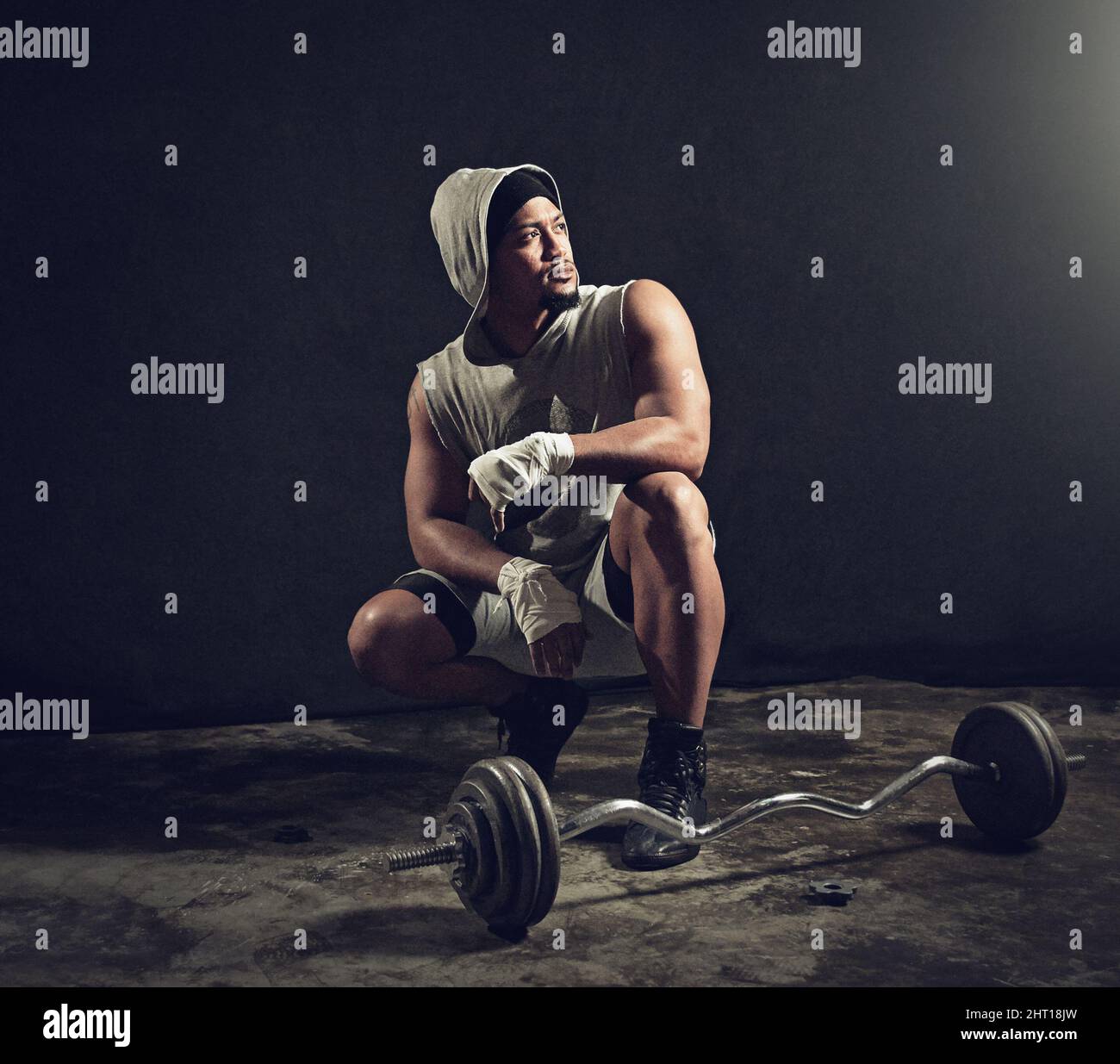 What a workout. Full length shot of an athletic young man crouching down besides weights against a dark background. Stock Photo