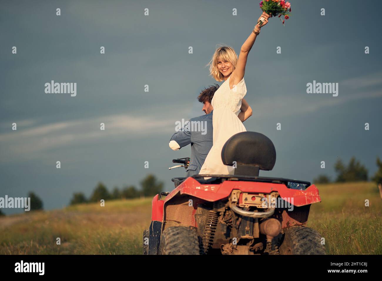 Joyful bride with bridal bouquet. Newlywed couple riding quad. Love, marriage, wedding, happiness, couple concept. Stock Photo
