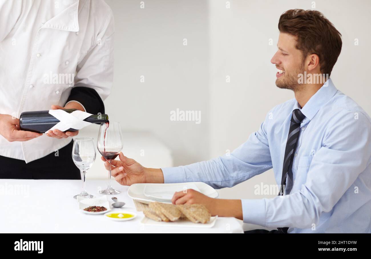 Ready to enjoy a great dining experience. Handsome young man smiling as a sommelier pours wine for him at a restaurant - Fine Dining. Stock Photo