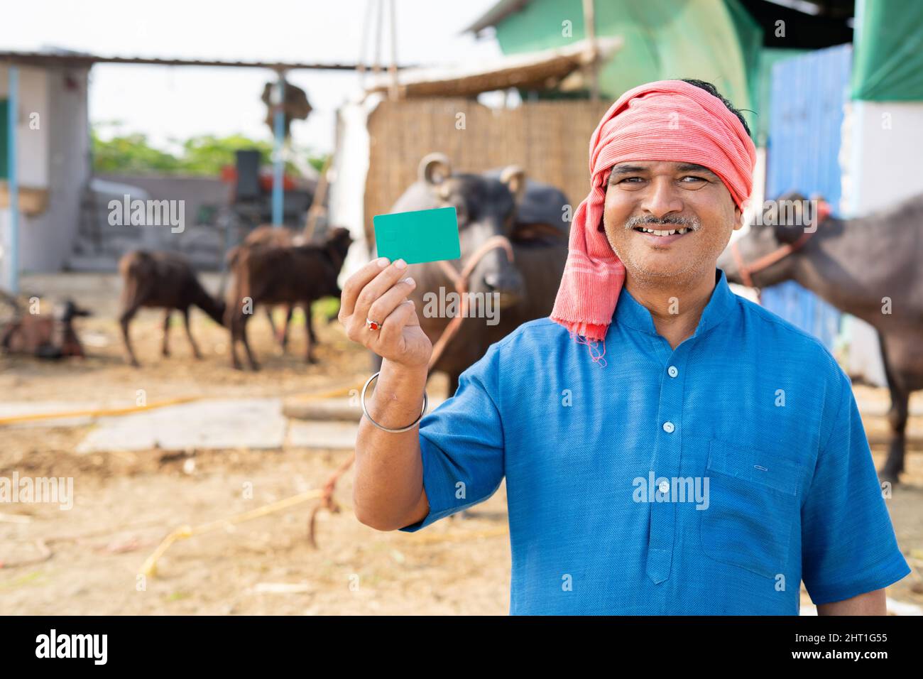 Smiling indian milk dairy farmer showing green card by looking at camera - concept of advertisement, promotions and successful Stock Photo