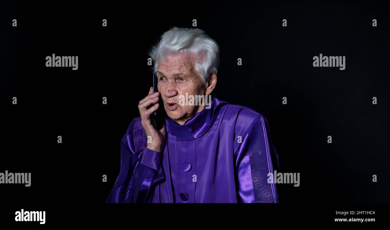 Elderly woman talking on a mobile phone on a black background Stock Photo