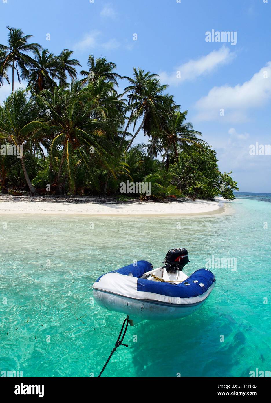 Dinghy tied to the back of boat in front of beautiful beach with clear