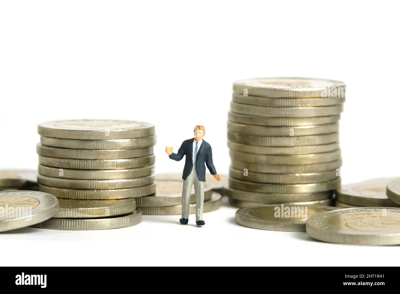Miniature people toy figure photography. Financial plan concept. A shrugging businessman standing in between two coin money stack. Isolated on white b Stock Photo
