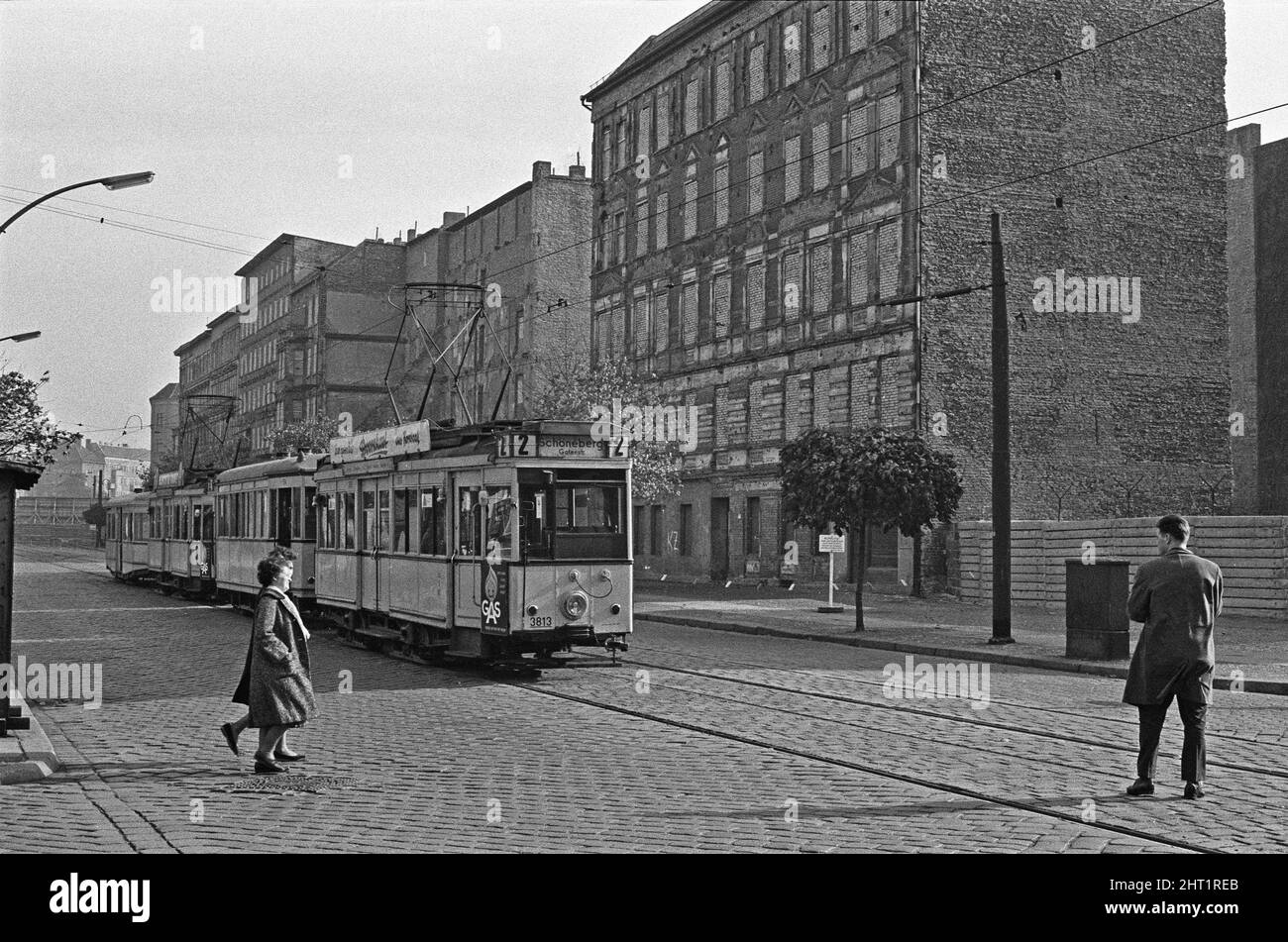 A tram runs along Bernauer Strasse, Berlin. The buildings on the east side of the street are in East Berlin, and the sidewalks and the street in West Berlin. Since this meant that a resident could walk out their front door to freedom, the East German authorities ordered the forcibly evacuation of all dwellings on the border and bricked up all the entrances and windows. Circa 1965 Stock Photo