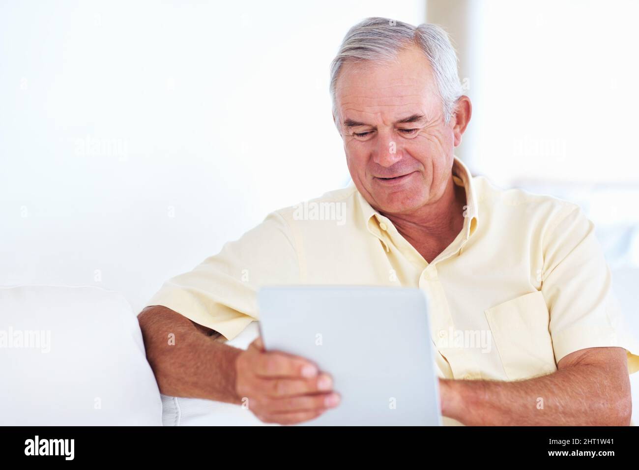 Mature man using tablet PC. Handsome mature man using tablet PC while sitting on couch. Stock Photo