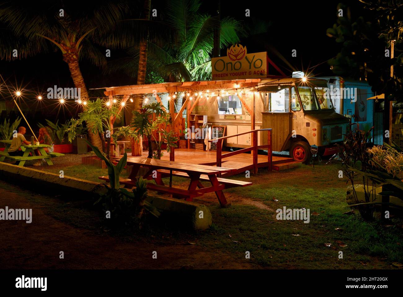 Food truck, strung lights and picnic tables, at night, selling tropical
