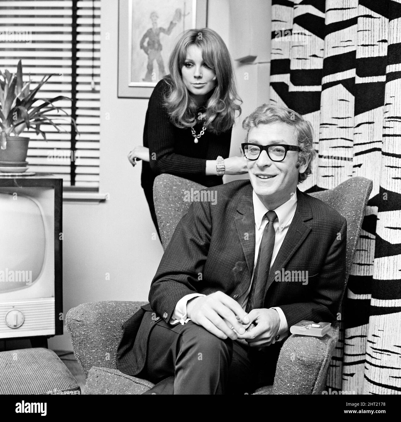 Actor Michael Caine pictured with French actress Miss Elizabeth Ercy in the flat of the Mirror's Donald Zec. 2nd December 1965. Stock Photo