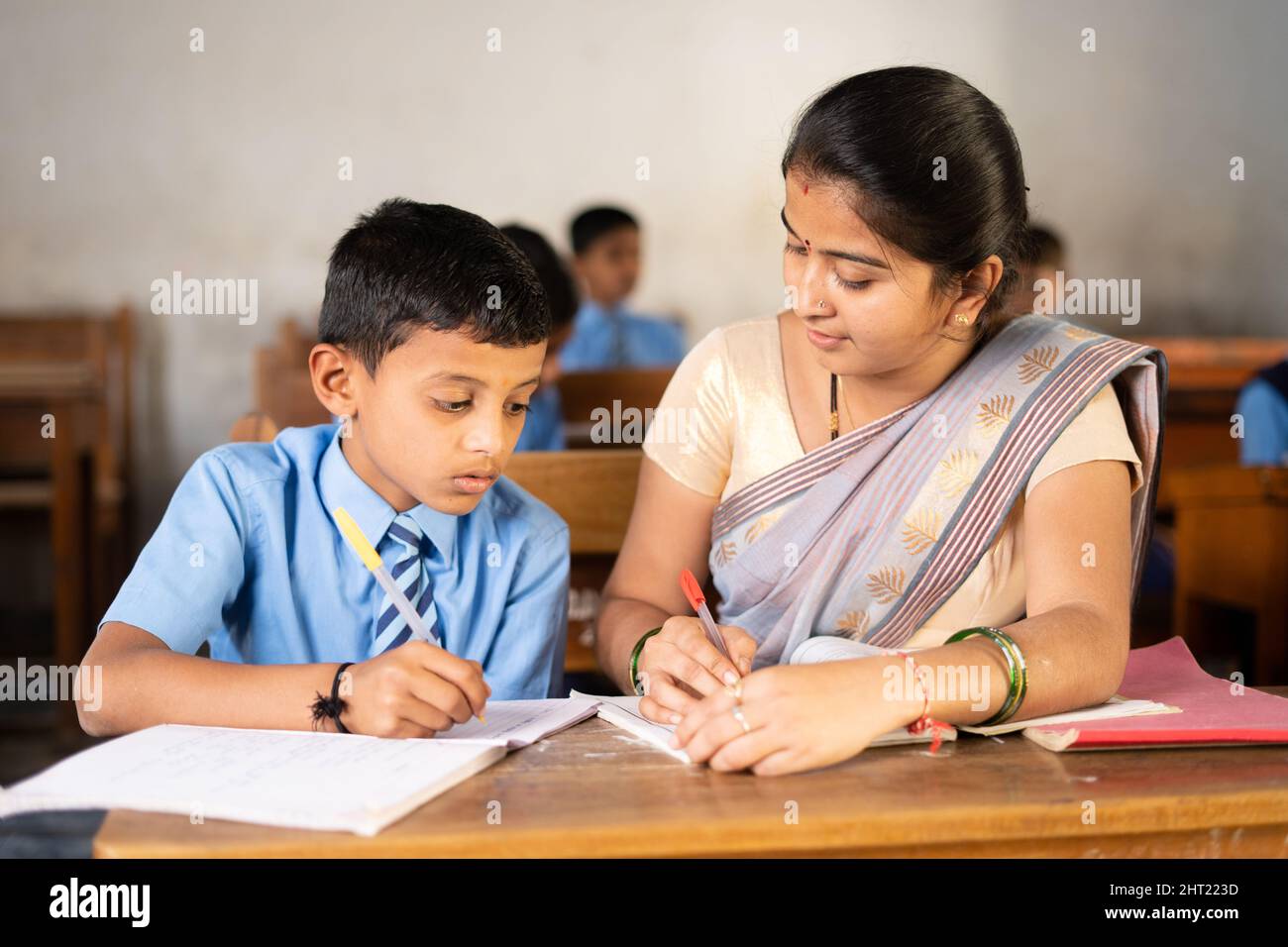 Teacher in classroom helping kid for studying at desk - concept of personal care, mentorship and coaching Stock Photo