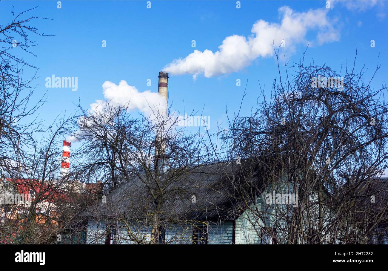 Chimneys of the plant, from which thick white smoke rises into the blue clear sky above the outskirts of the city. Air pollution . Exhaust gases, ozon Stock Photo