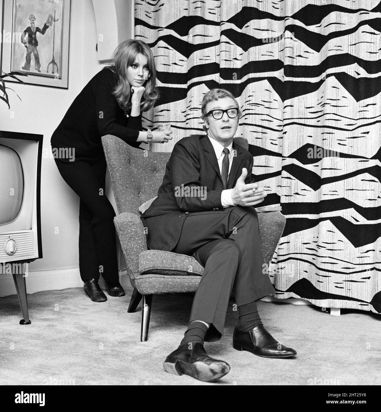 Actor Michael Caine pictured with French actress Miss Elizabeth Ercy in the flat of the Mirror's Donald Zec.  2nd December 1965. Stock Photo