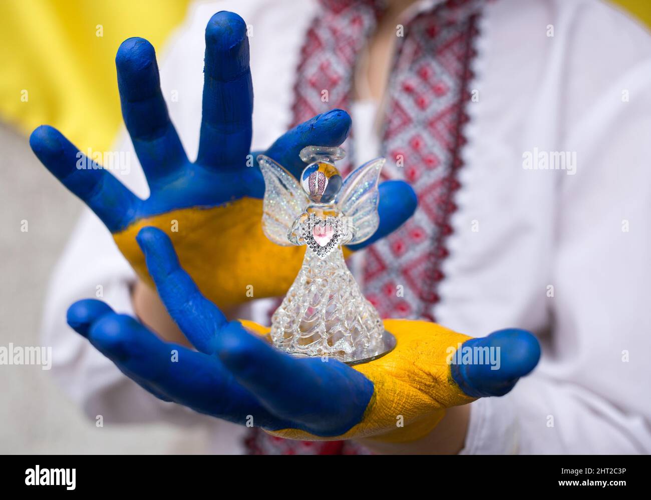 children's hands, painted in yellow and blue, hold a glass angel. Children against war. Russia's invasion of Ukraine, a request for help from world co Stock Photo