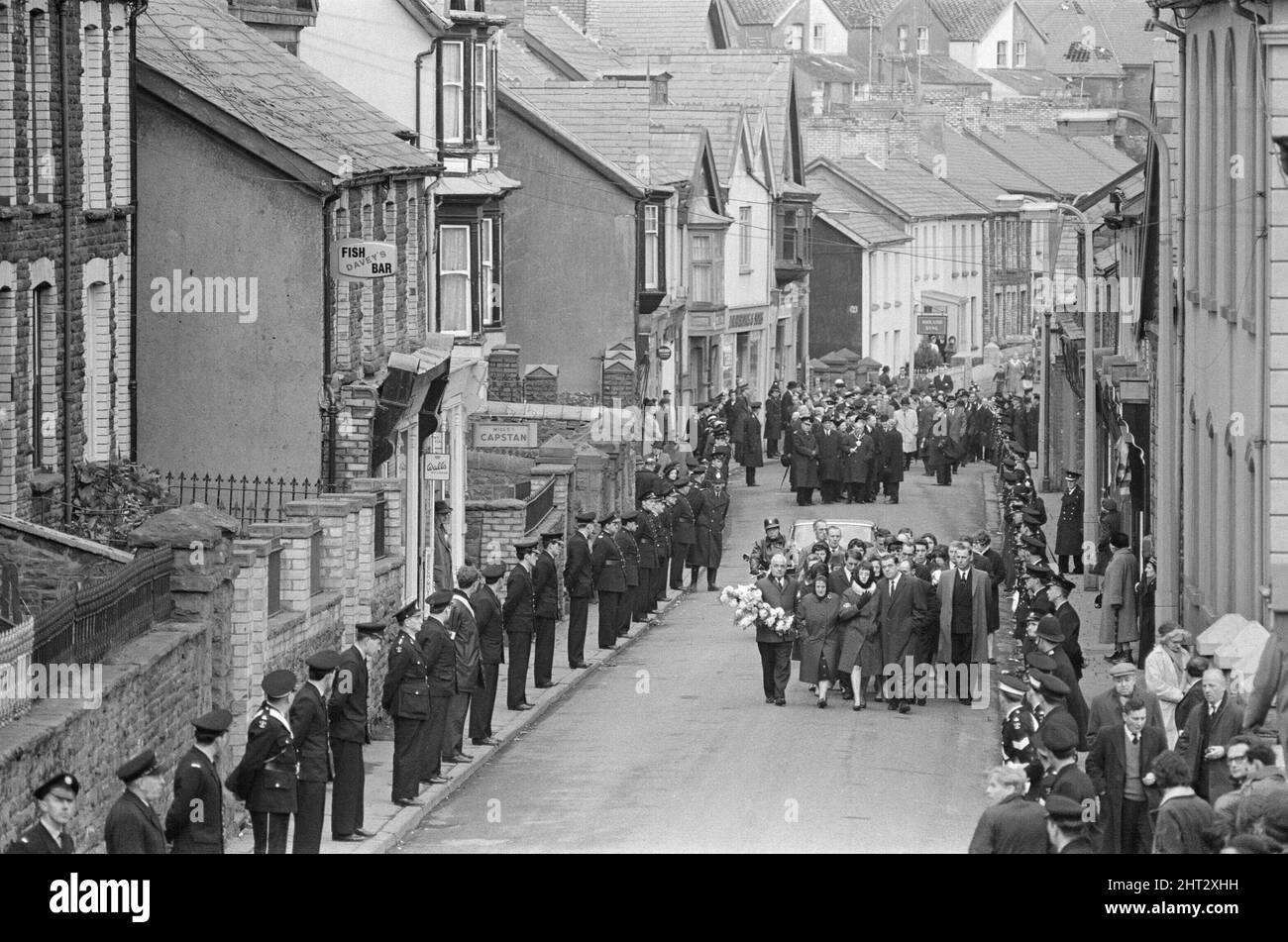 Aberfan - 27th October 1966.  Mourners walk through the streets, on their way to the cemetery to attend the mass funeral for victims of the Aberfan mud slide disaster. The streets are lined with members of the emergency services as a mark of respect.  The Aberfan disaster was a catastrophic collapse of a colliery spoil tip in the Welsh village of Aberfan, near Merthyr Tydfil. It was caused by a build-up of water in the accumulated rock and shale, which suddenly started to slide downhill in the form of slurry and engulfed The Pantglas Junior School below, on 21st October 1966, killing 116 child Stock Photo
