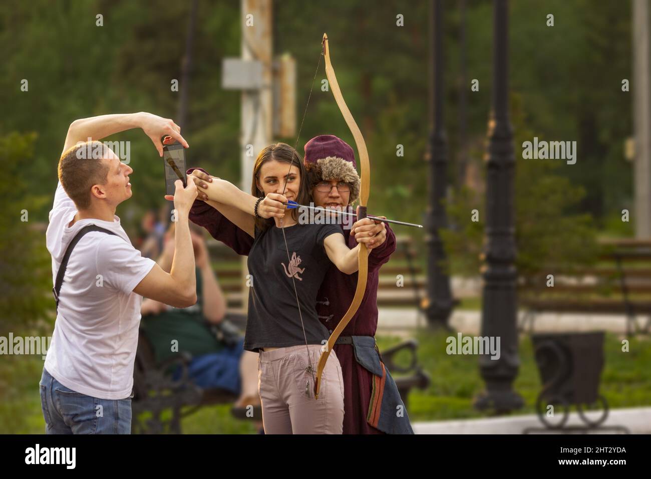 Omsk, Russia. 9 May, 2021. Preparing for a mass archery flash mob. The guy takes a picture on the phone of his girlfriend with an archery bow and a tr Stock Photo