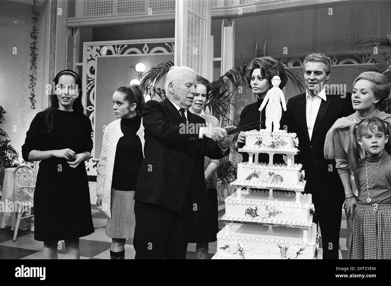 Actor and director Charlie Chaplin legend of the silent movies celebrates his 77th birthday on the set at Pinewood where he is making a new film 'Countess from Hong Kong'. Pictured, Charlie Chaplin cutting his cake with Sophia Loren, Sydney Chaplin (Chaplin's son), Tippi Hedren and her daughter Melanie Griffith. 15th April 1966. Stock Photo