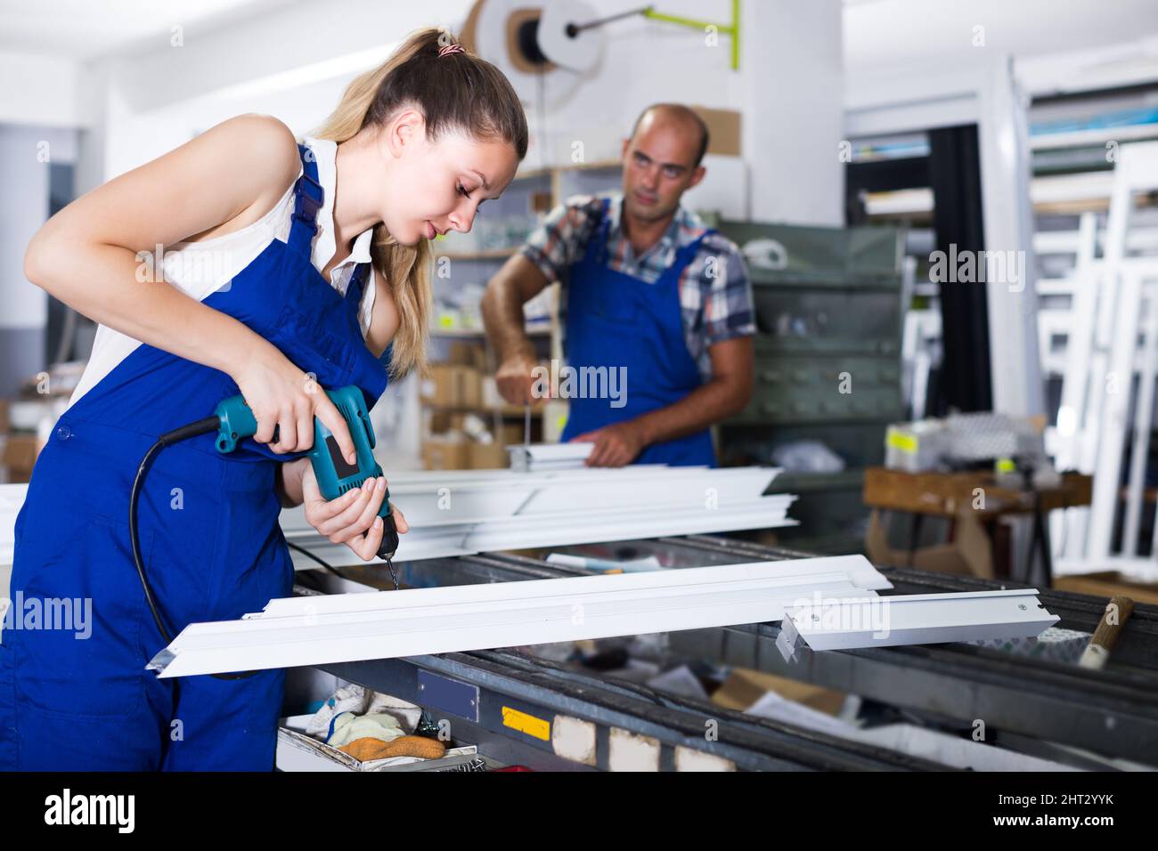 Craftswoman is assembling metal-plastic window using electric drill. Stock Photo