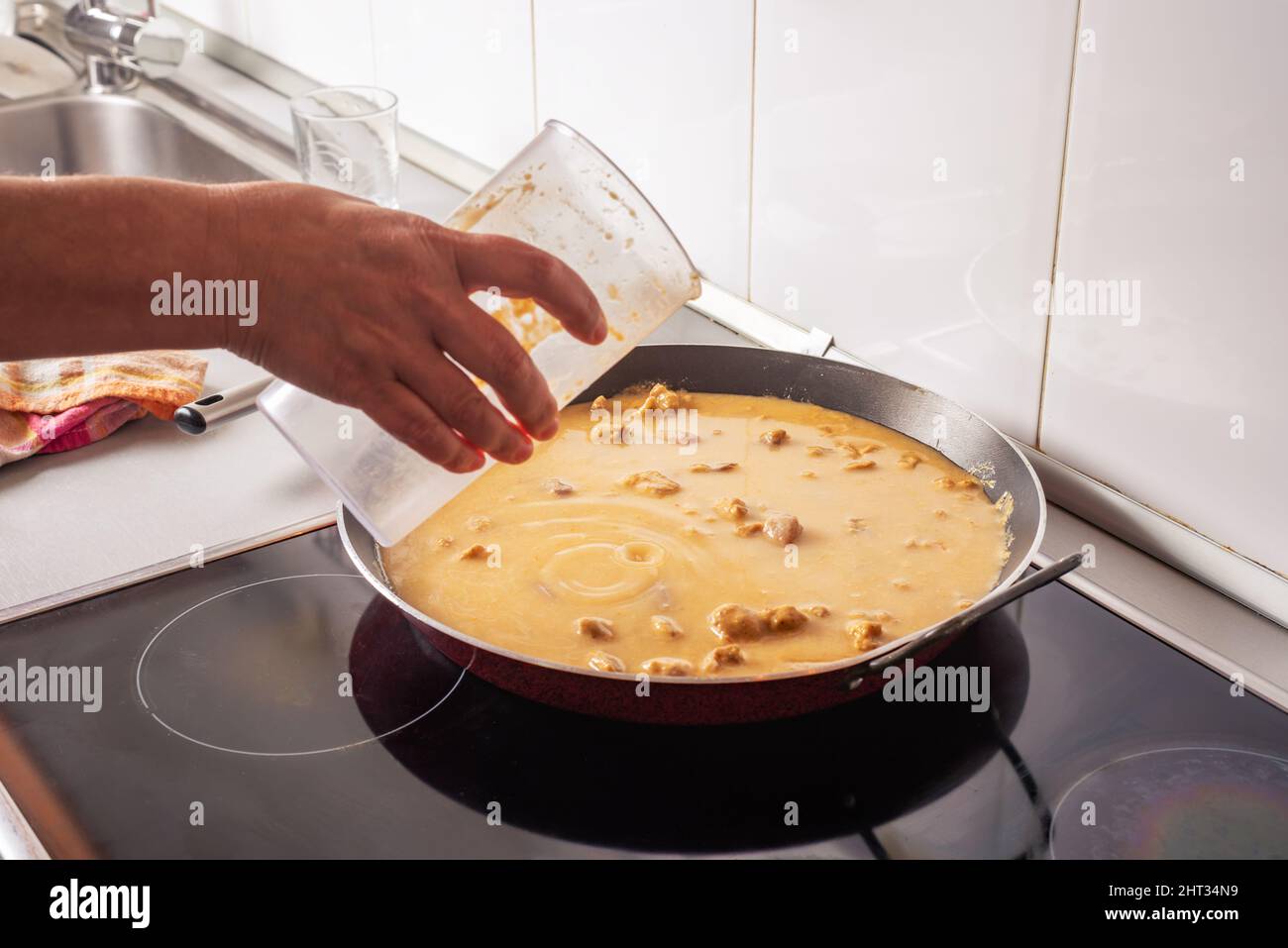 A woman's hand pouring the sauté into the pan to make a paella. Stock Photo