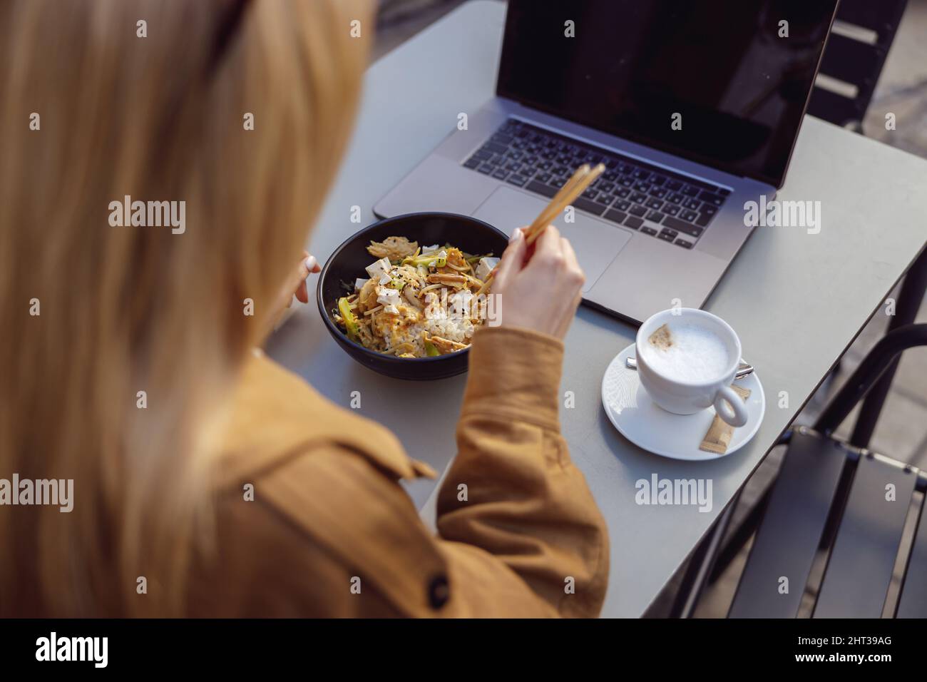 Back photo of lady sitting at street cafe table holding chopsticks Stock Photo