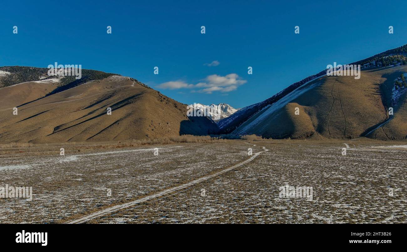 Snow covered mountain peaks are distant with a road leading Stock Photo ...