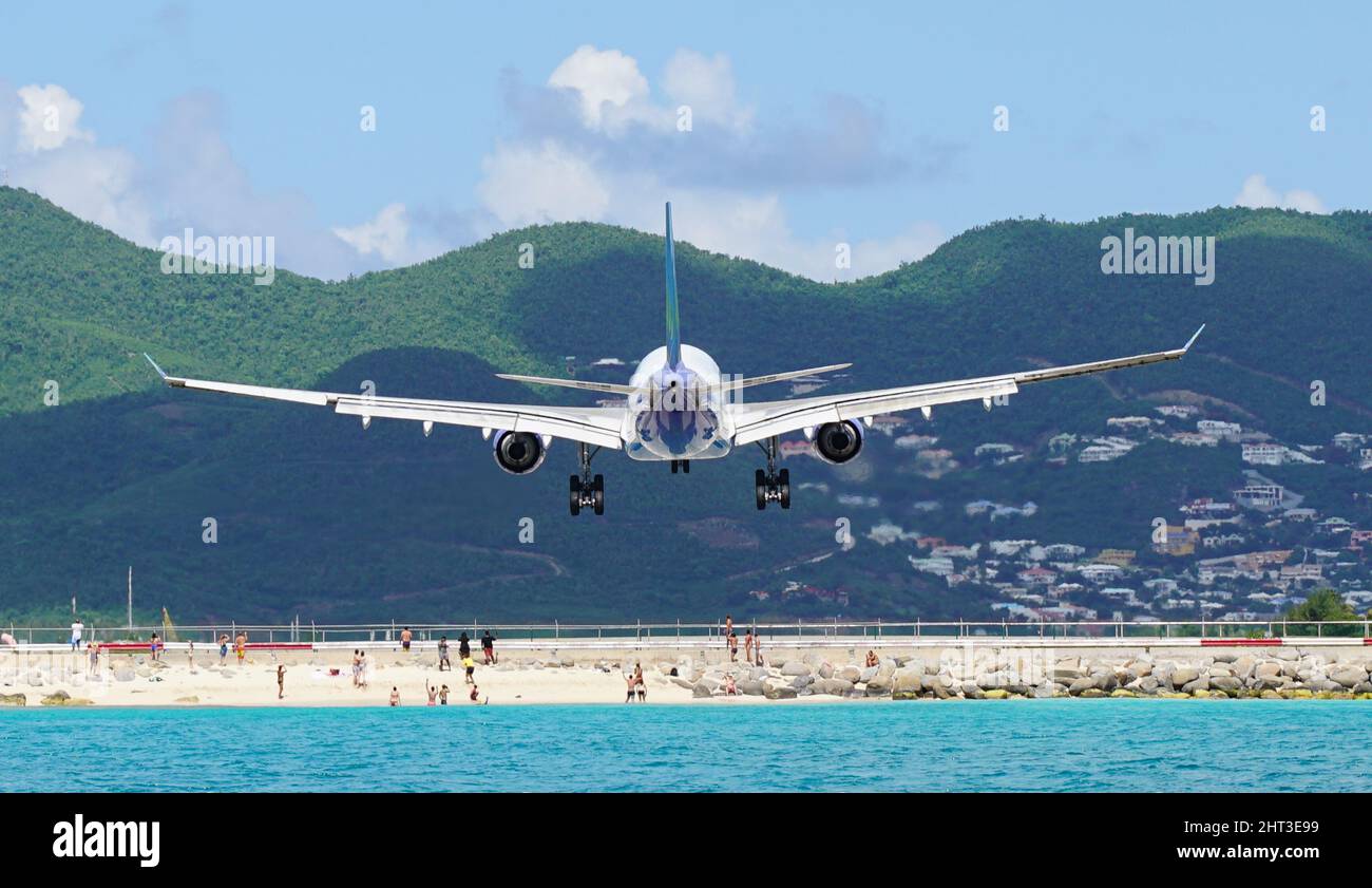 Airplane flying over people during landing at Maho Beach in Saint Maarten at Princess Juliana airport. Unique view of commercial plane landing. Stock Photo