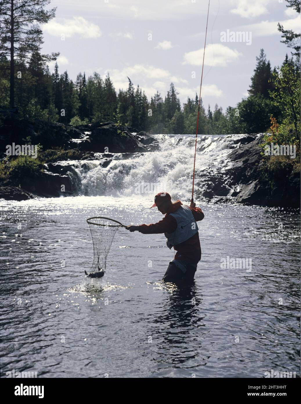 Woman with fish catch in front of waterfall Stock Photo