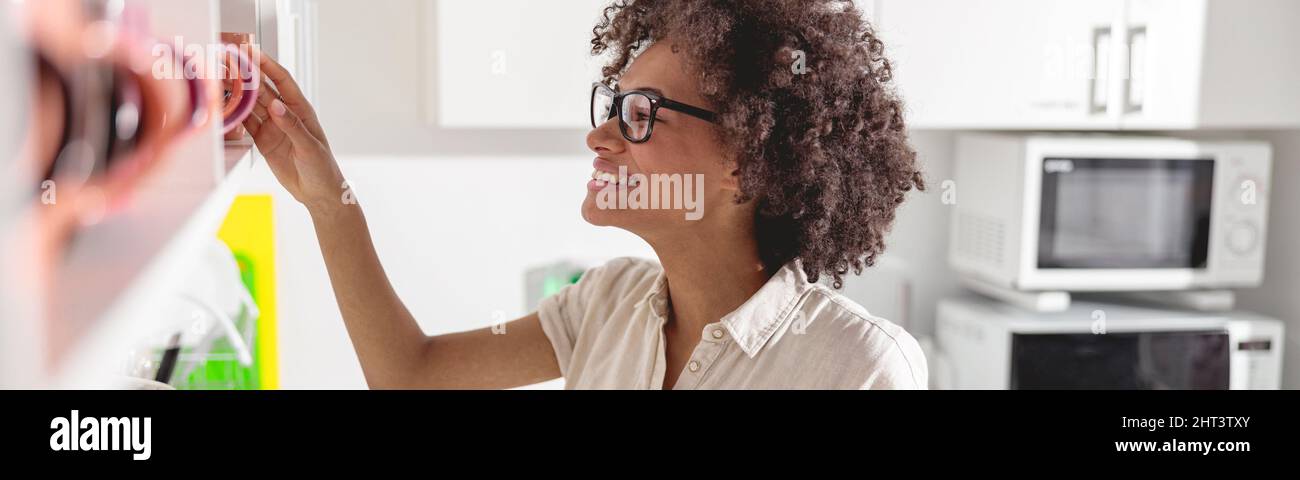 Happy Afro American lady taking a cup off the shelf Stock Photo