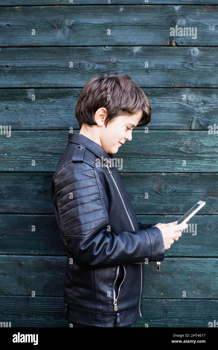 A vertical shot of a young boy looking at a tablet near a green wall Stock Photo