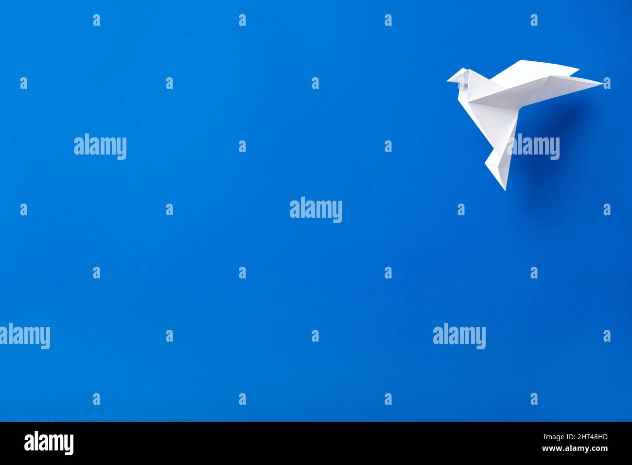 White origami paper dove flying against a blue background. Stock Photo