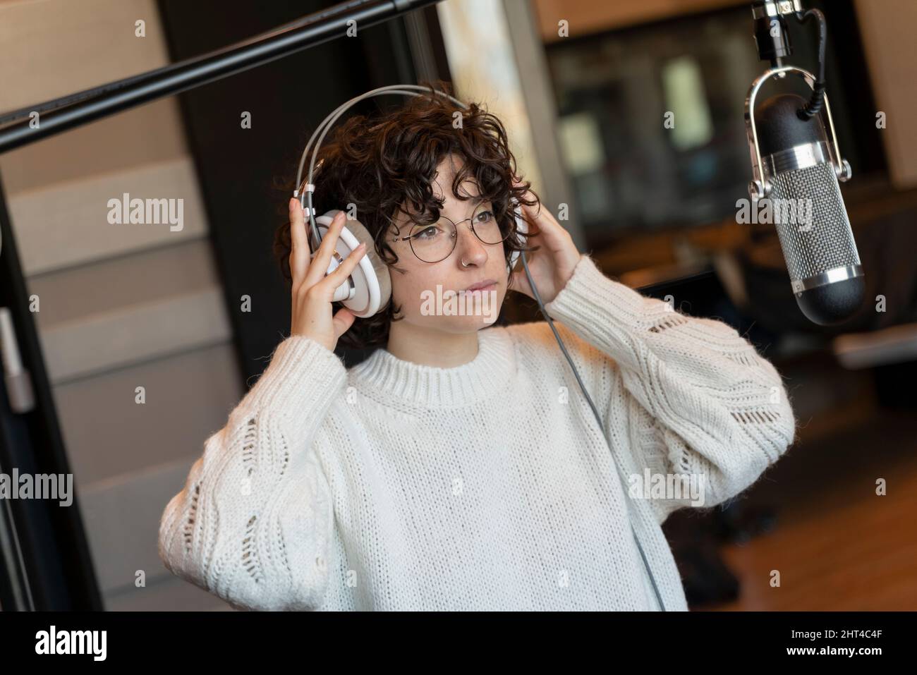 A young curly hair singer woman with glasses recording a song in a real