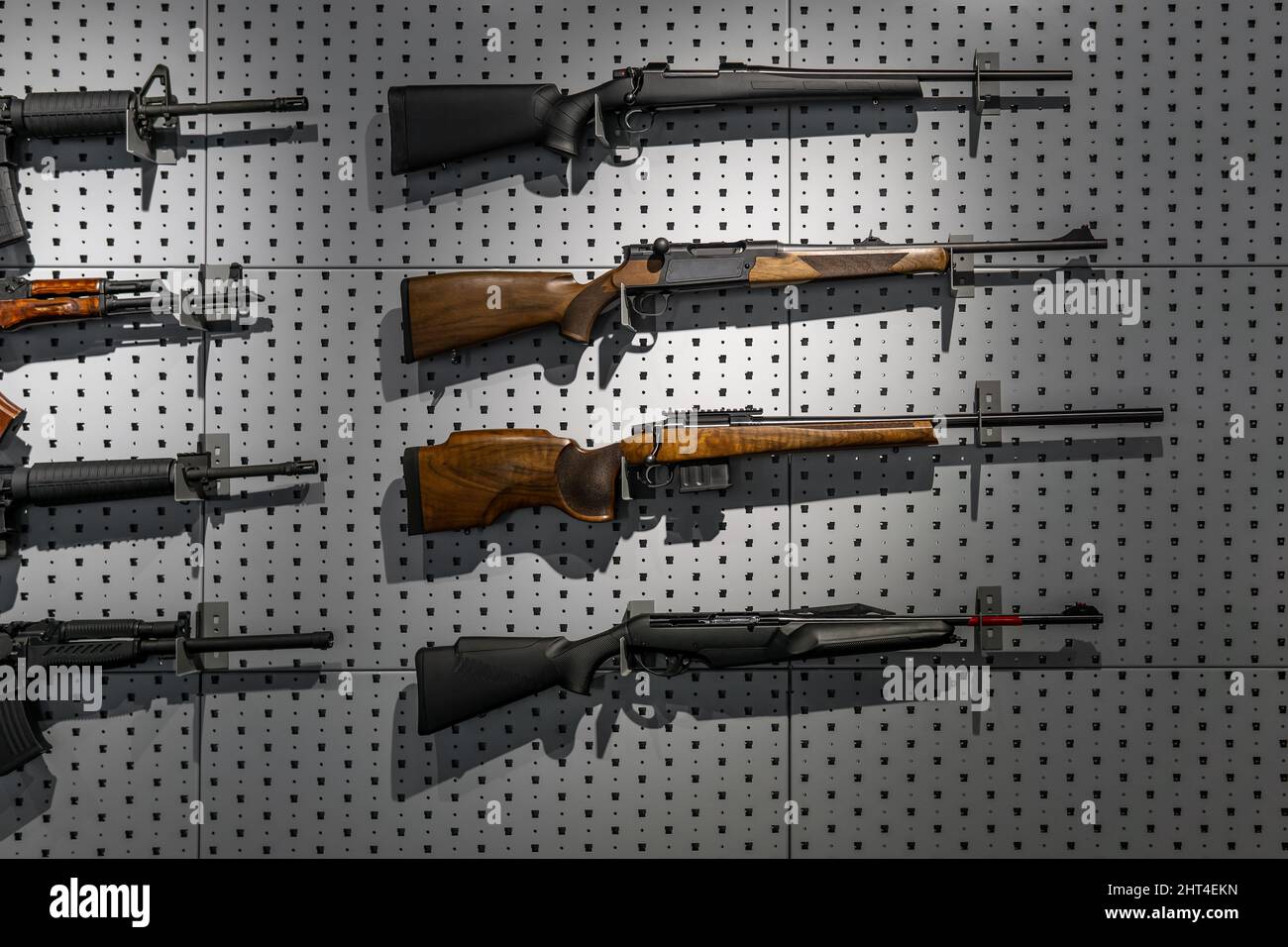 Collection of rifles and carbines. Various firearms hang on special mounts on the wall. Weapon background. Stock Photo