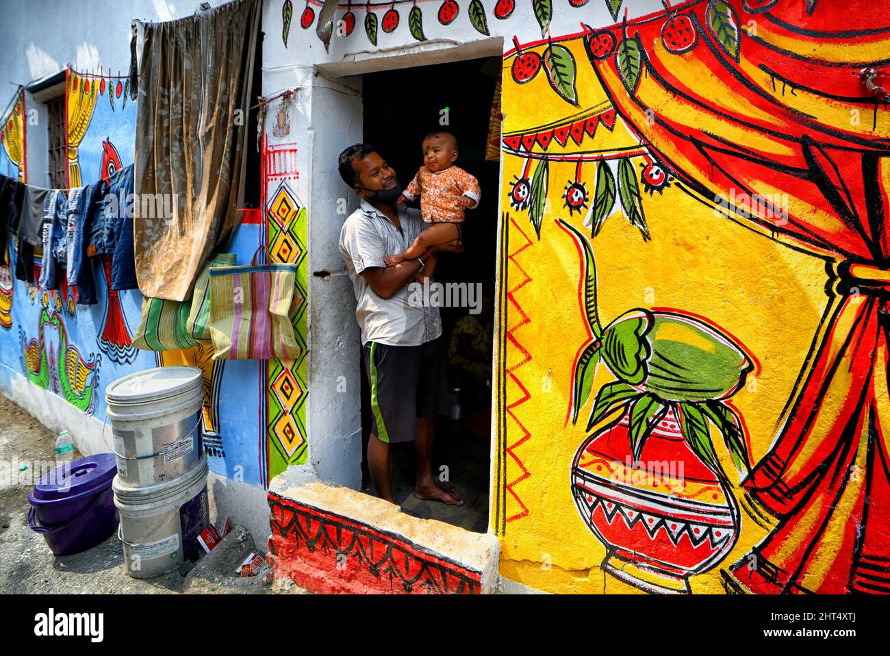 A man seen carrying a baby in a colorful slum surroundings with ...