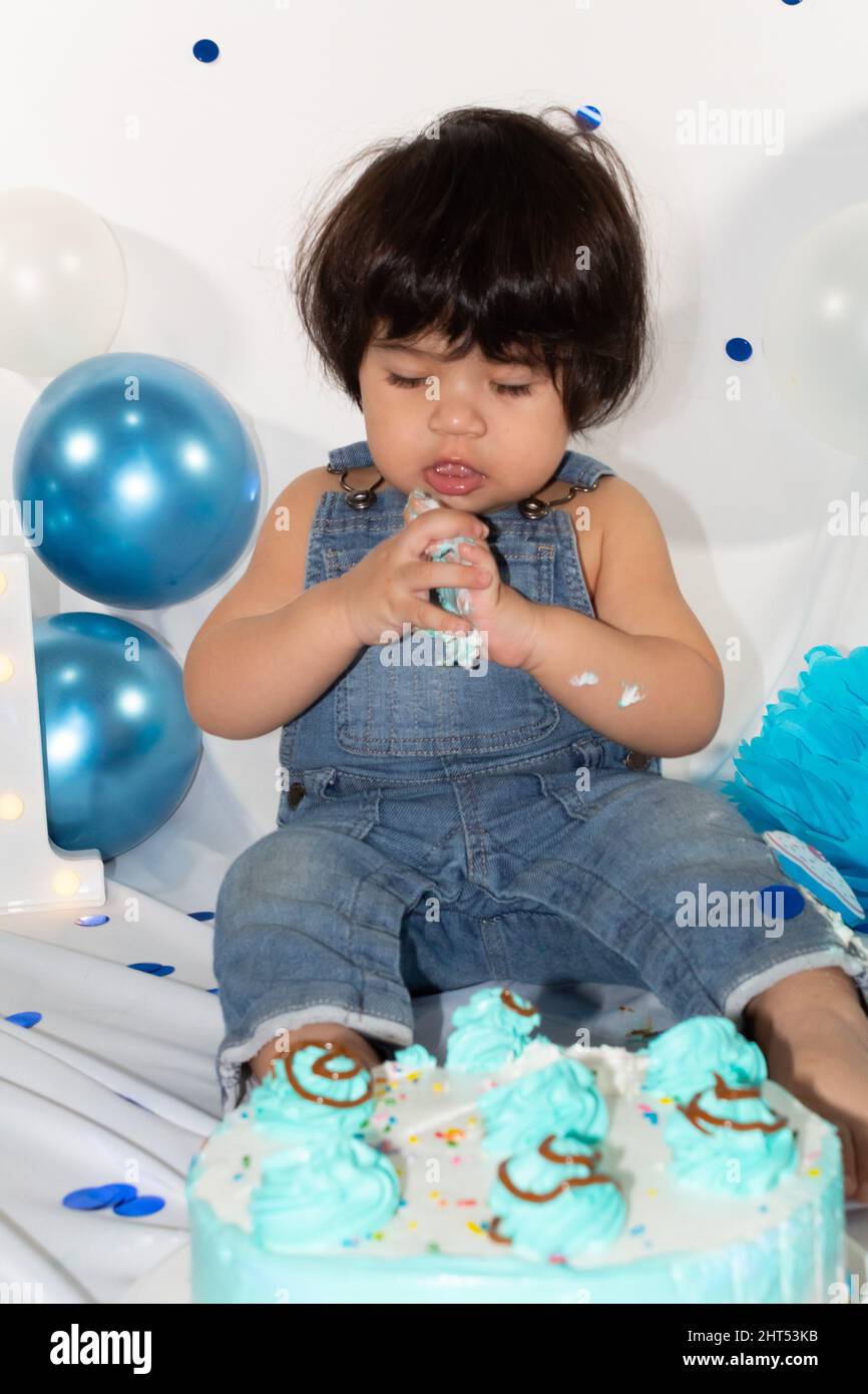birthday photo session of a hispanic baby with overalls eating cake