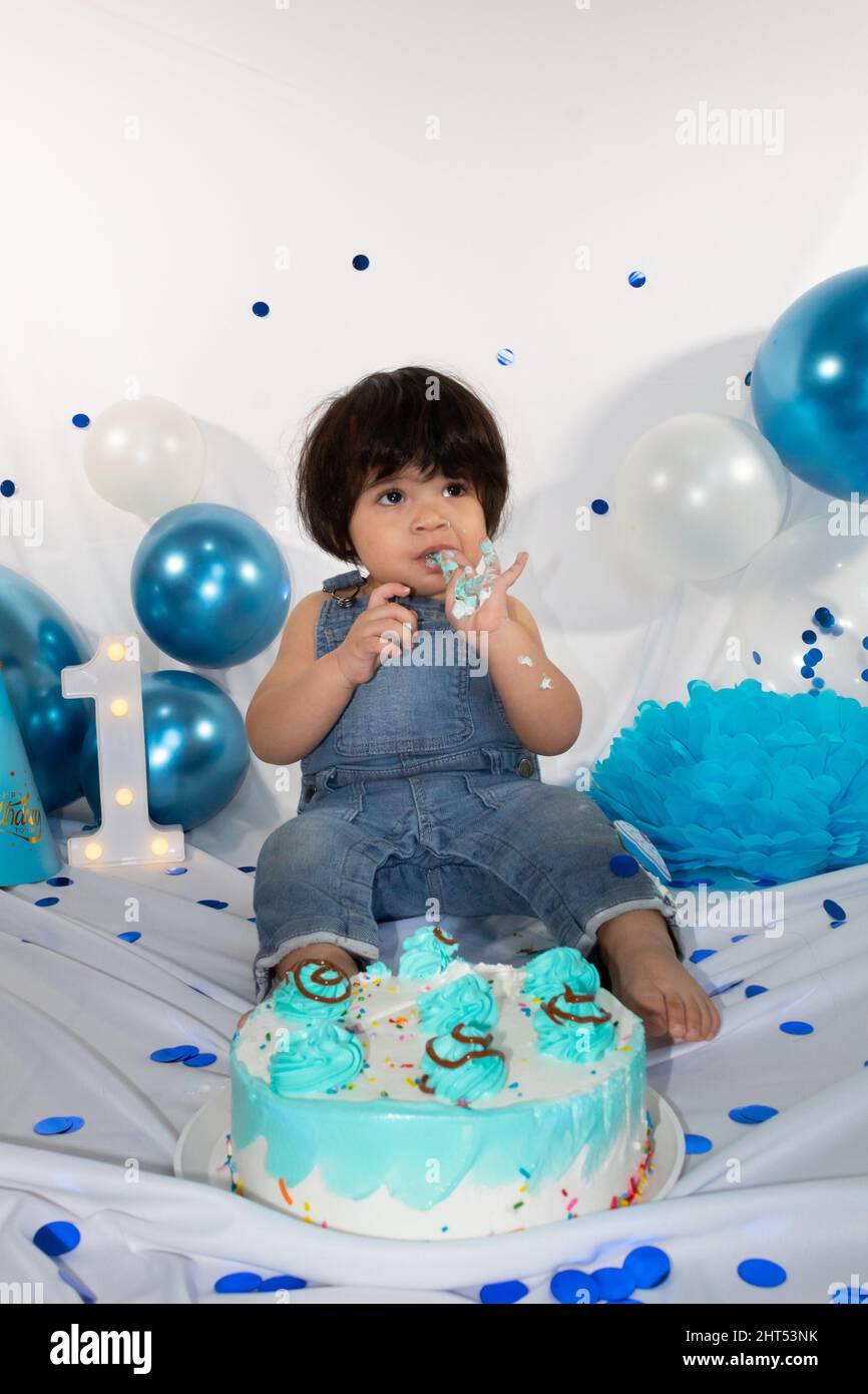 birthday photo session of a hispanic baby with overalls eating cake