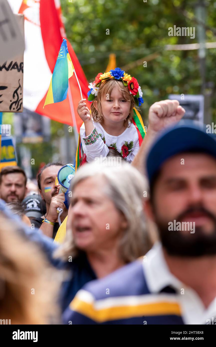 Melbourne, Australia, 27 February, 2022. A young girl with flowers in her hair is carried as she holds a Ukrainian flag during a protest in support of the people and the government of Ukraine in the face of a Russian invasion. Speakers prayed, and called for weapons to the be supplied to Ukraine and the intervention of NATO and the Untied Nations, Melbourne. Credit: Michael Currie/Speed Media/Alamy Live News Stock Photo