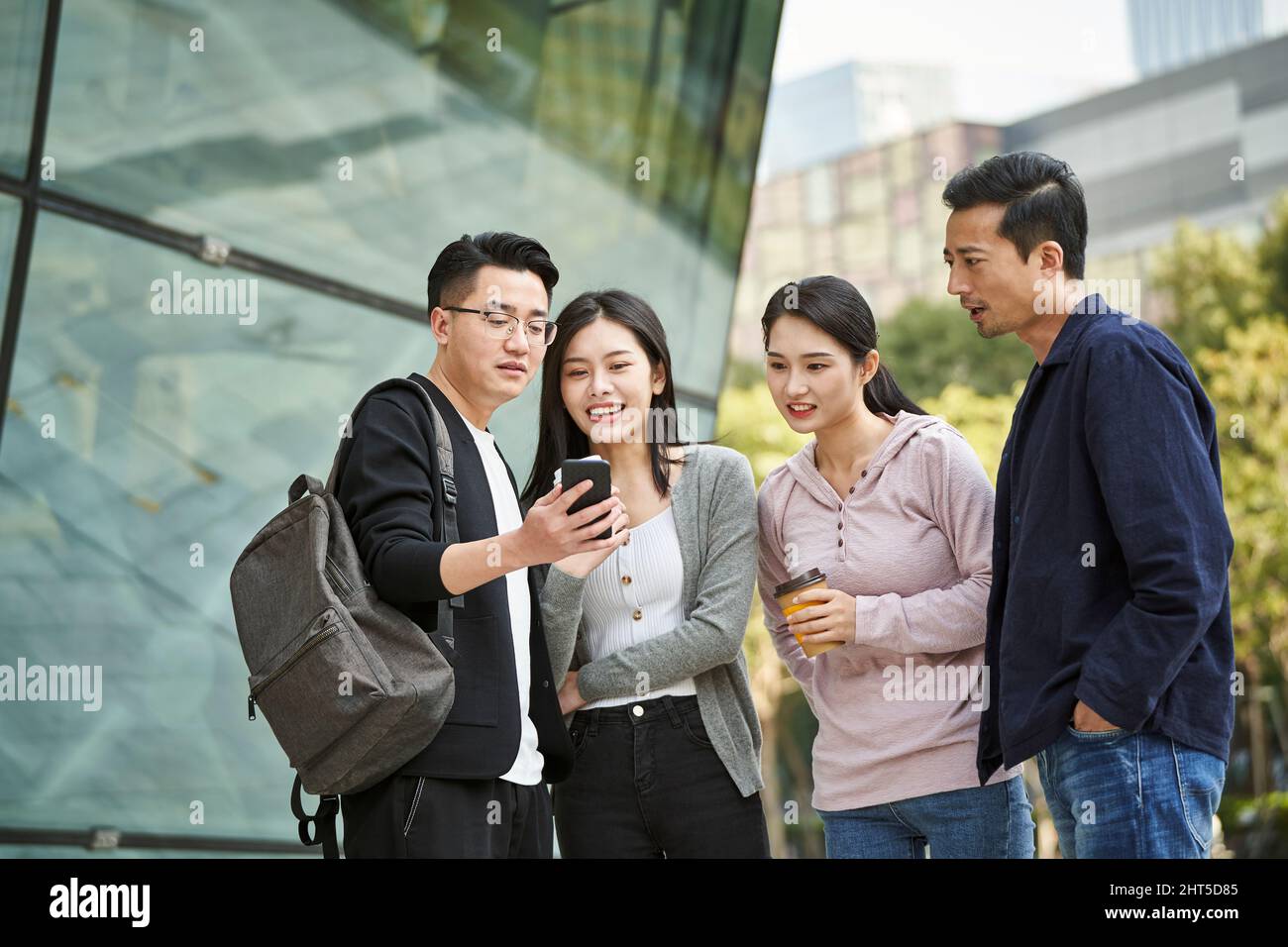 group of young asian people looking at cellphone together outdoors happy and smiling Stock Photo