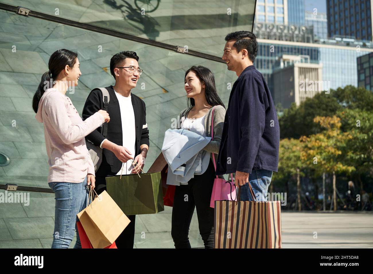 group of four young asian people standing on street talking chatting conversing during shopping trip happy and smiling Stock Photo