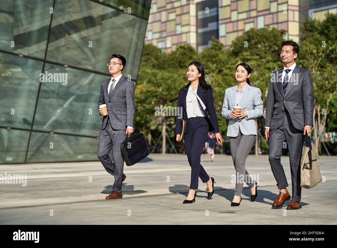 group of four young asian business people walking outdoors on street in modern city Stock Photo