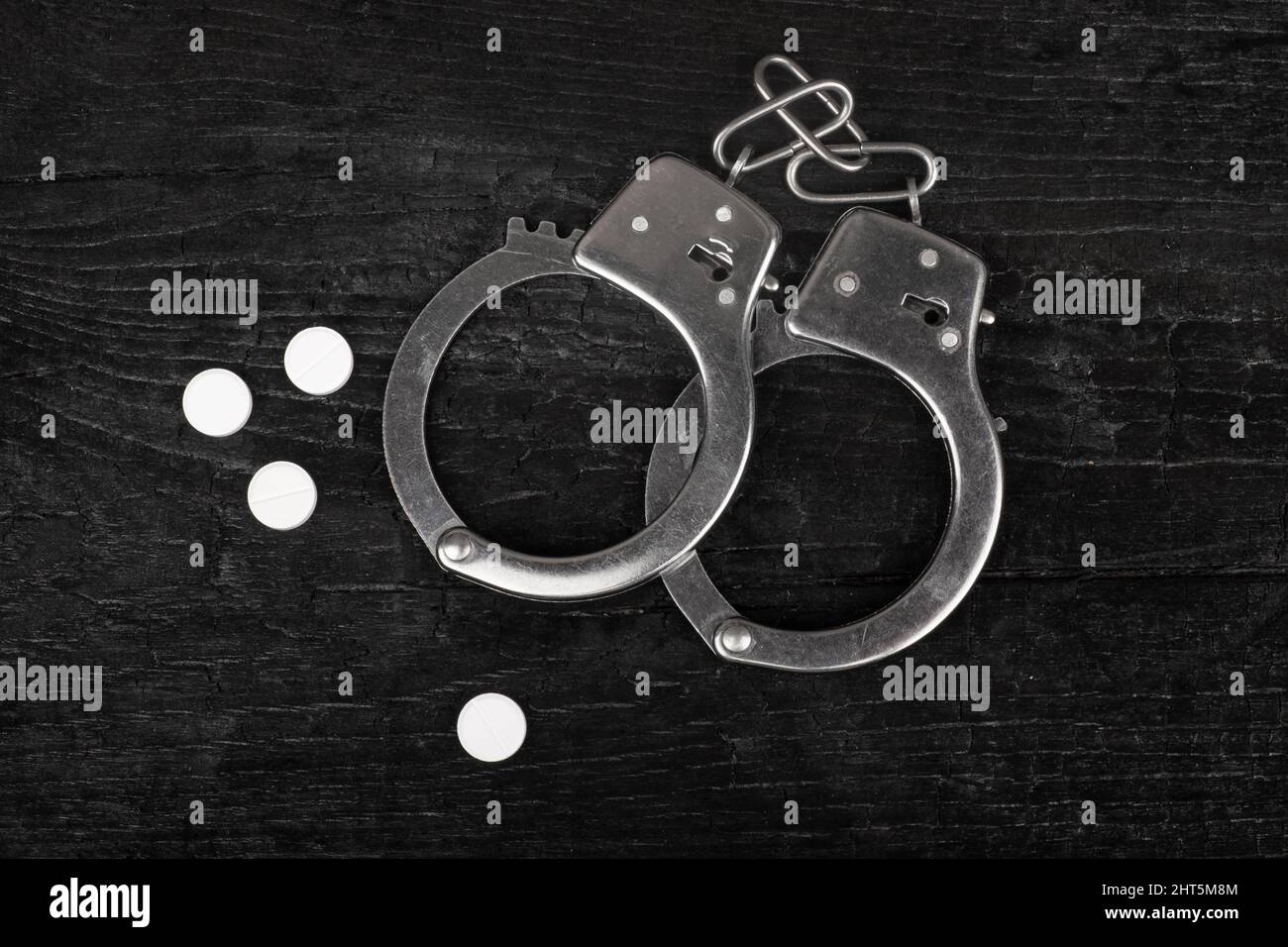 metal handcuffs on a black background with white narcotic pills. Stock Photo