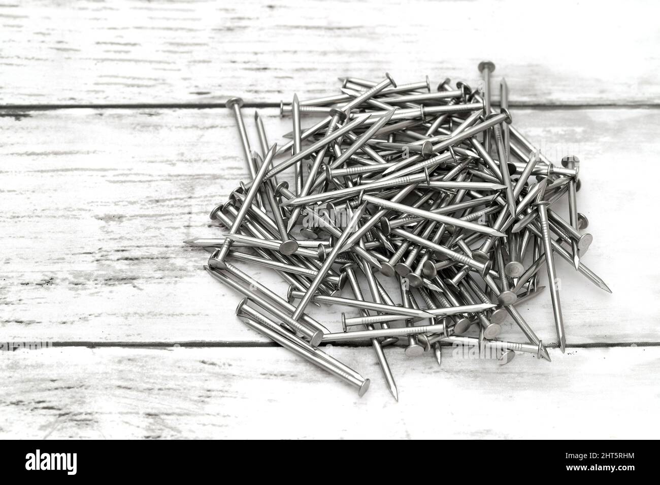 Pile of silver metallic nails on white wooden background Stock Photo