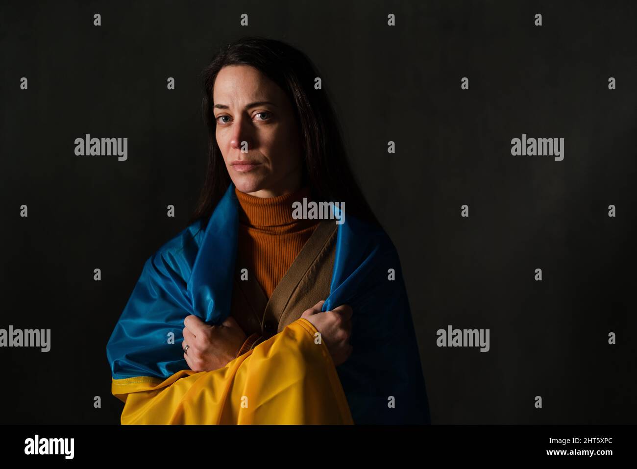 Sad woman covered with Ukraine flag. Concept of standing with Ukrainian nation in war with Russia. Stock Photo