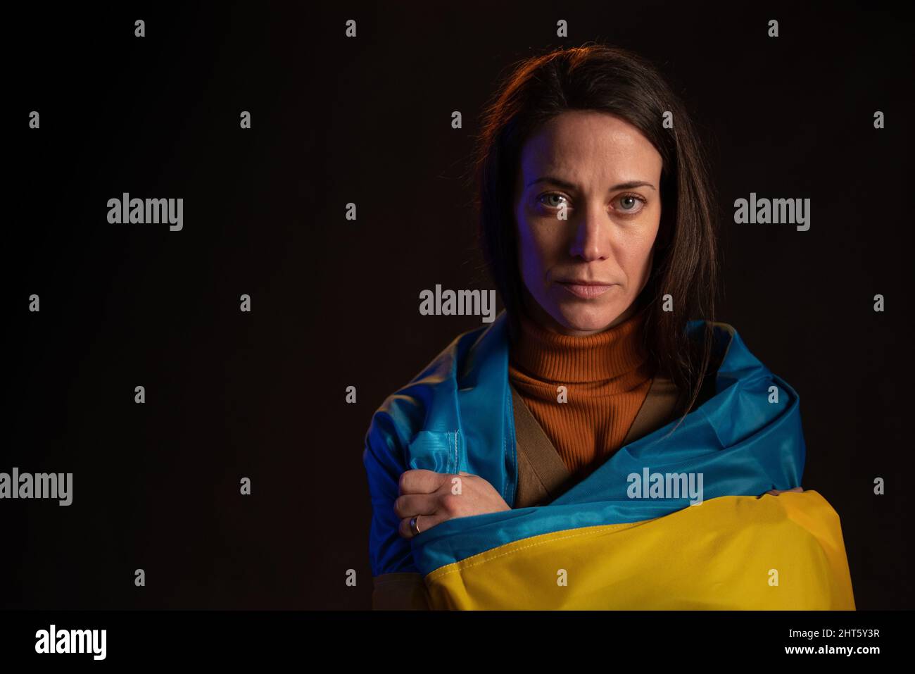Sad woman covered with Ukraine flag. Concept of standing with Ukrainian nation in war with Russia. Stock Photo