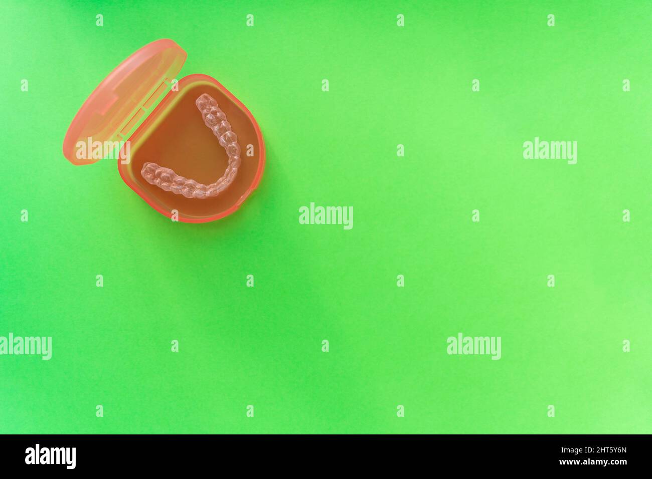 Transparent tooth aligner in red case on green background Stock Photo