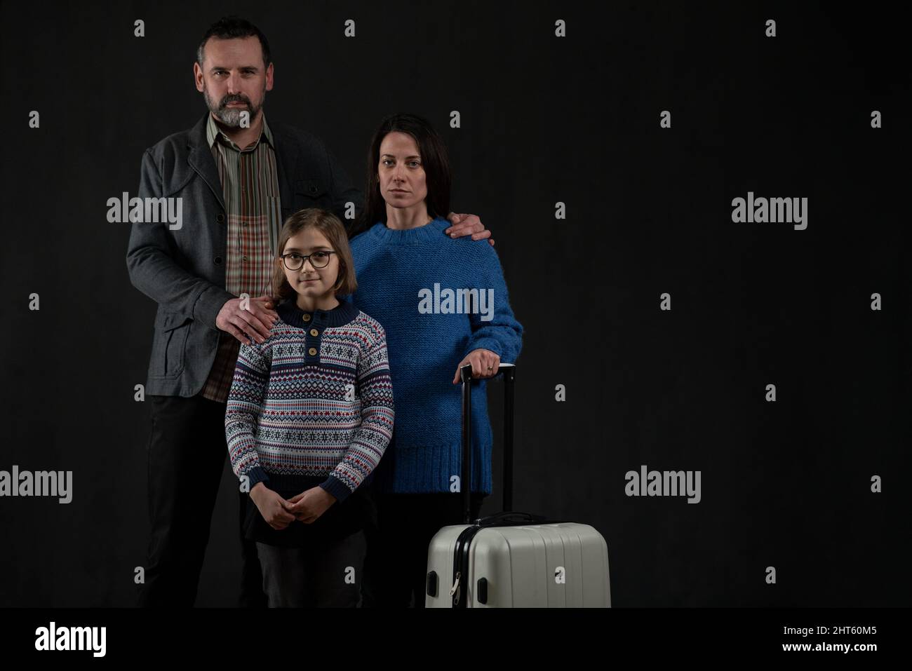 Refugee family with one child looking at camera on black background, Ukraine war concept. Stock Photo