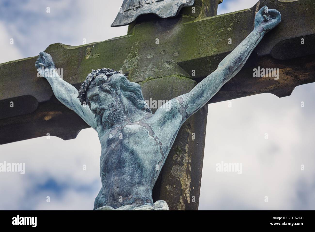 Cross with a crucified figure of Jesus Christ. Close up of Jesus Christ against the background of blue sky. Old, stone cross in the summer. Stock Photo