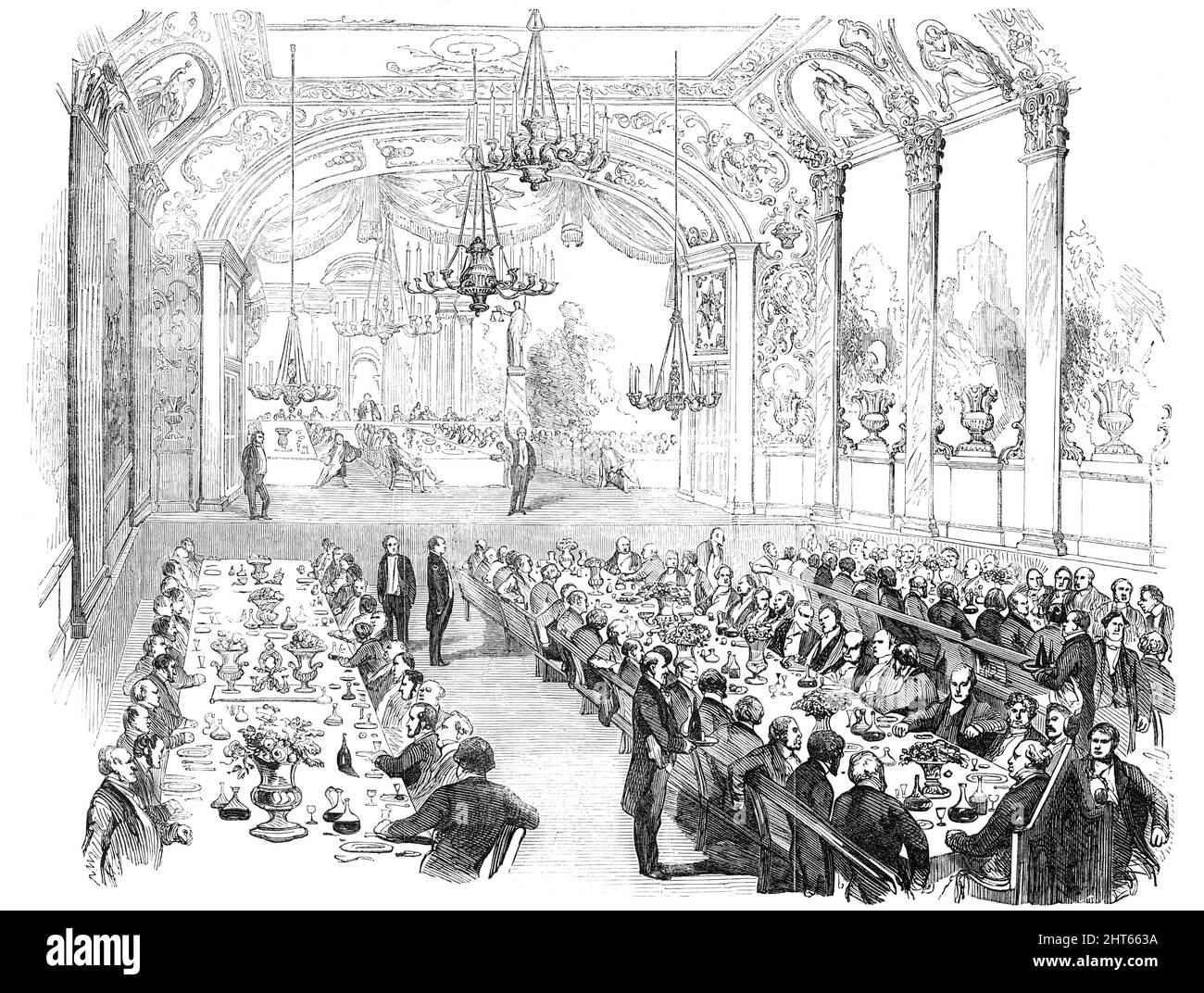 Reform Banquet in the Theatre, Wellington, New Zealand, 1850. 'Nearly two hundred guests sat down to a sumptuous dinner...On the stage was the chairman's table, from which three tables extended...towards the footlights...The stage was embellished with flags, evergreens, &amp;c. A new scene, painted by Mr. Marriott, expressly for the occasion, tapestried the wall behind the chair; representing a Roman arch, flanked by columns, and surmounted by figures of Justice and Victory. The whole of the theatre and the staircase leading to the stage were hung with chandeliers of lights, whose brilliance s Stock Photo
