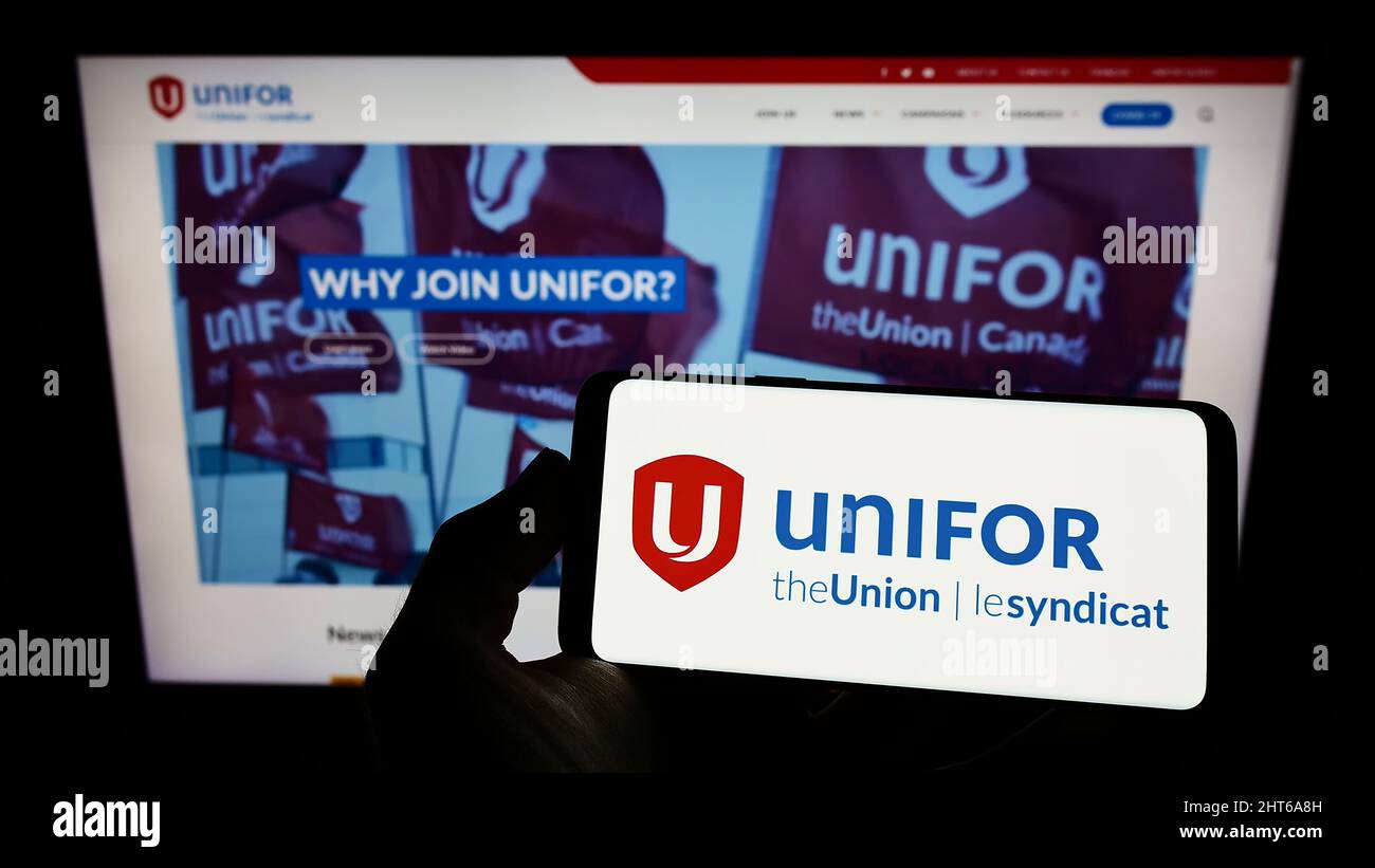 Person holding smartphone with logo of Canadian general trade union Unifor on screen in front of website. Focus on phone display. Stock Photo