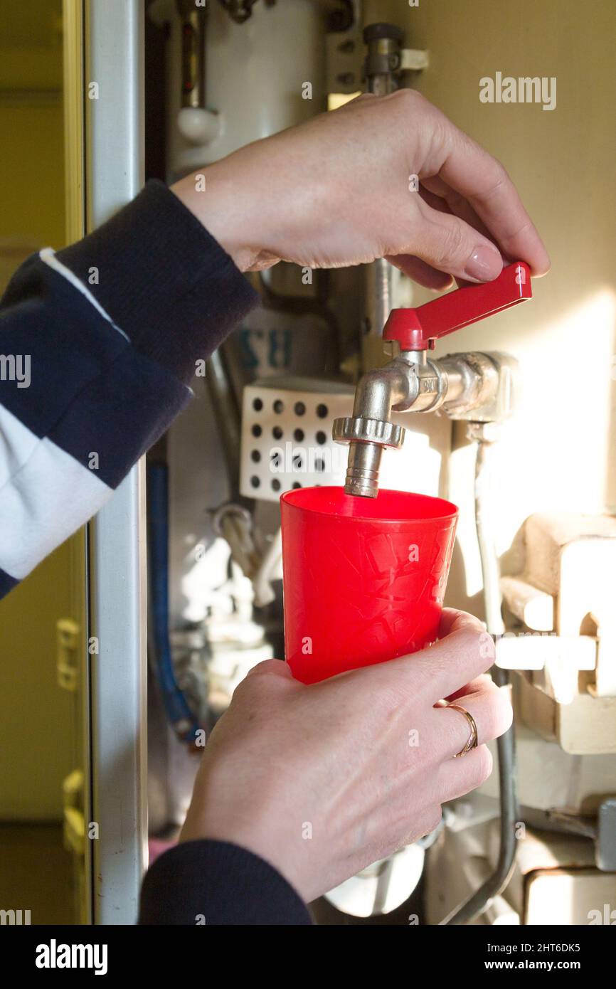 A woman's hand pouring boiling water into a red glass train car Stock