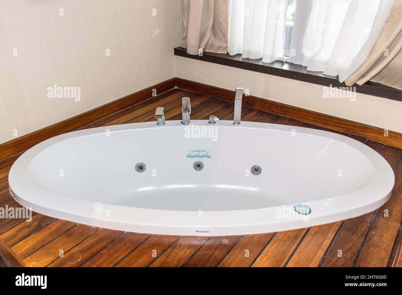 Hot tub with wooden side flooring next to a window Stock Photo