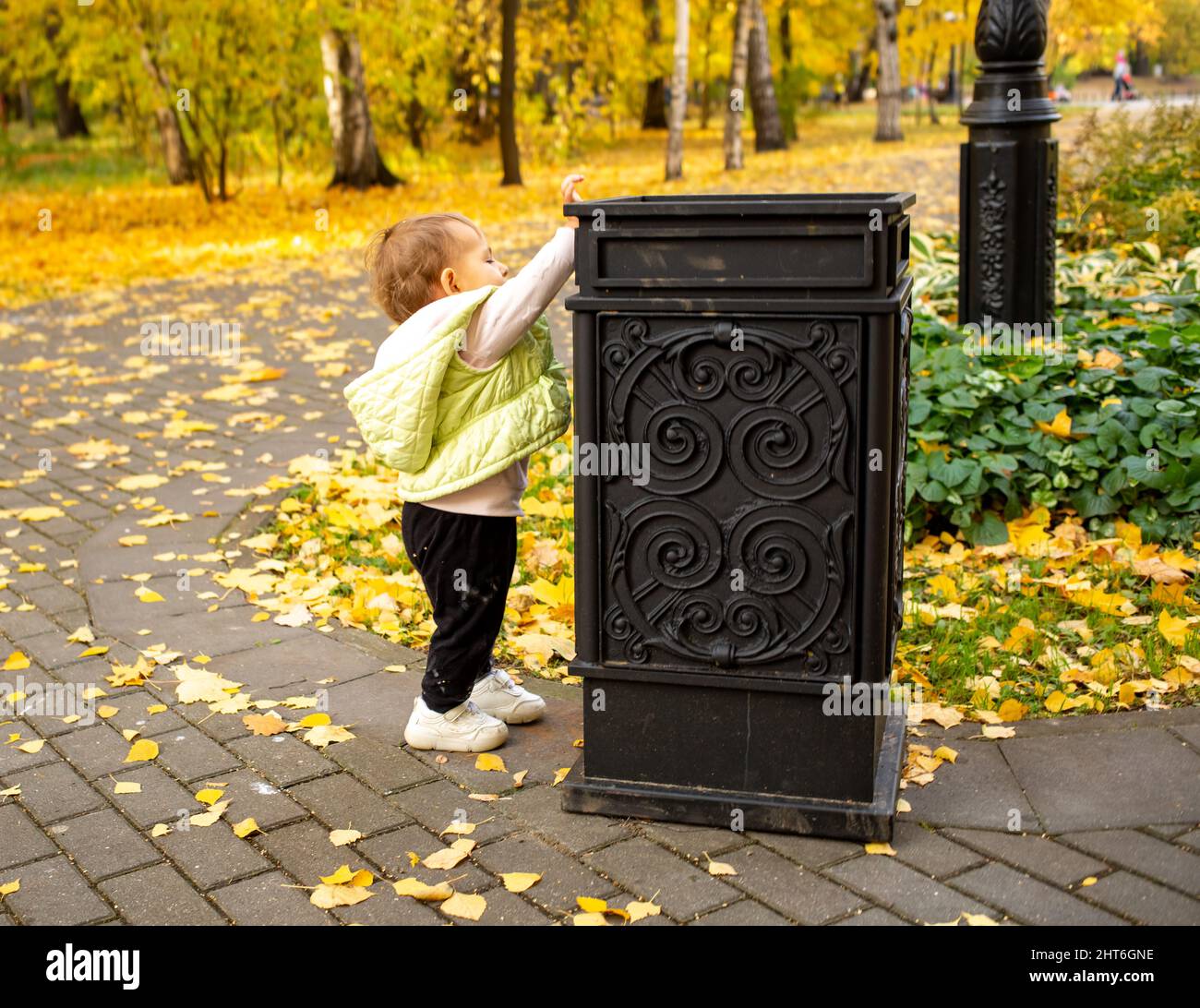 cute little baby throws trash into trash can in autumn park. instilling cultural norms from birth Stock Photo