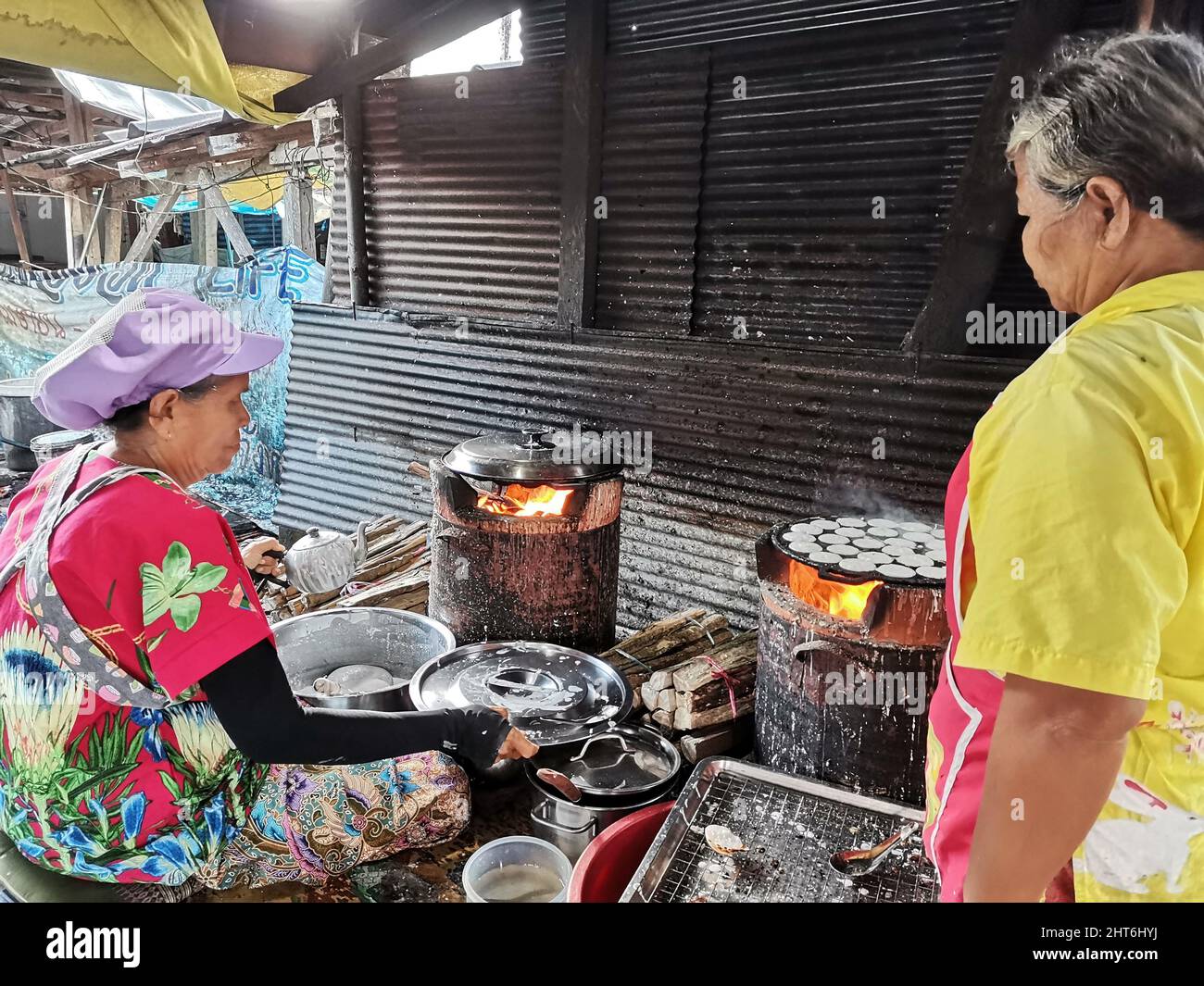 Thai old women and sister people work and cook sweet meal traditional kind of thai sweetmeat Kanom Krok or thai coconut pancakes pastry for sale at lo Stock Photo