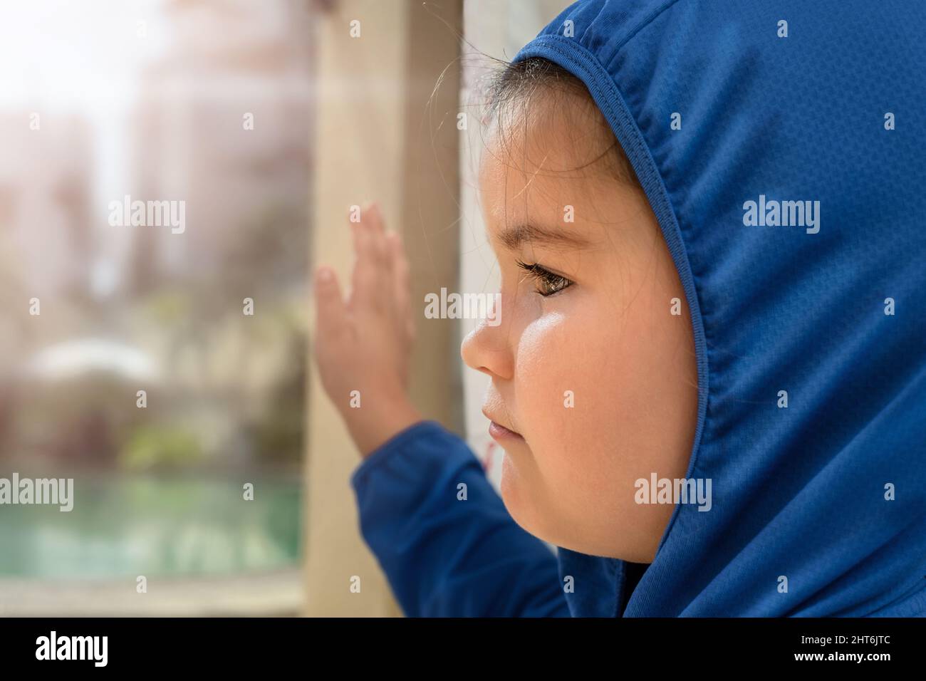 Sad child looks out the window with her hand on the glass Stock Photo